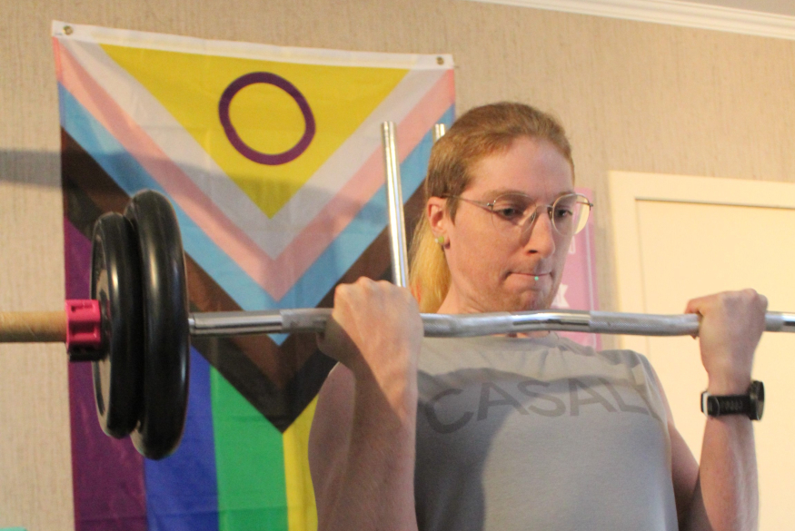 Intersekse sporter Bella draagt een gewicht met de Intersex Progress Pride vlag op de achtergrond