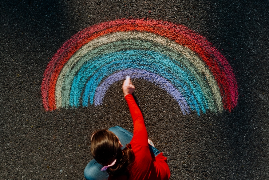 Persoon tekent regenboog op de straat met krijt