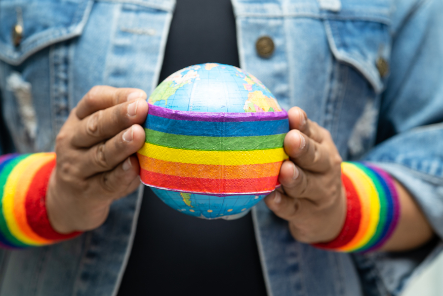 persoon die aardbol vastheeft met regenboogband en rond de polsen twee regenboogbanden heeft