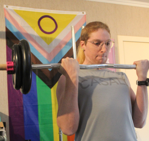 Intersekse sporter Bella draagt een gewicht met de Intersex Progress Pride vlag op de achtergrond