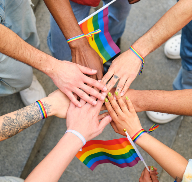 Zeven handen op elkaar met regenboogvlaggen ernaast. 