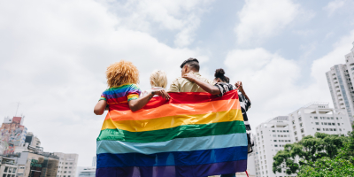 Verschillende mensen staan op een rij met de regenboogvlag rond hen gewikkeld