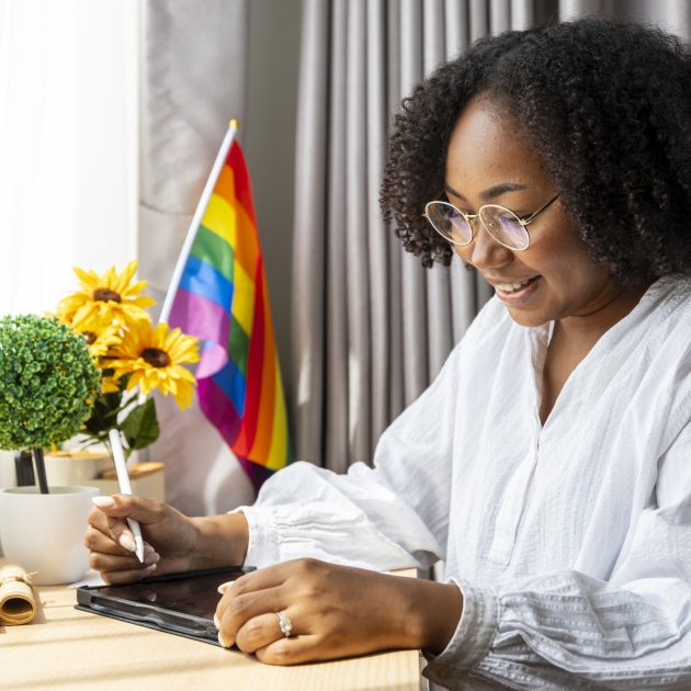 persoon die aan bureau zit met een regenboogvlagje op de achtergrond