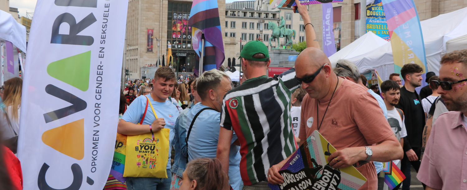 Groep personen op Pride, met bannervlag van çavaria en bord met 'laat je horen'