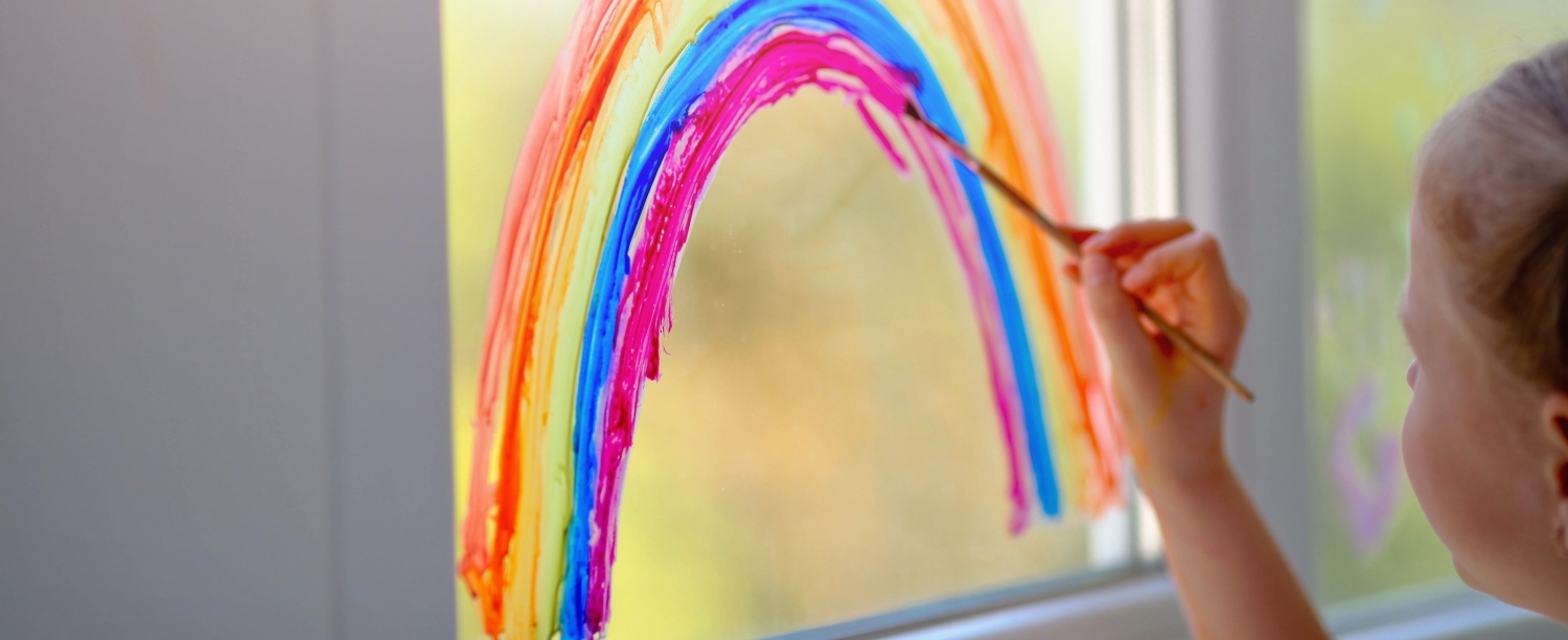 een kind schildert een regenboog op een ruit