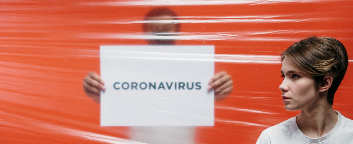 persoon in wit tshirt achter plastiek folie met bord ''coronavirus'