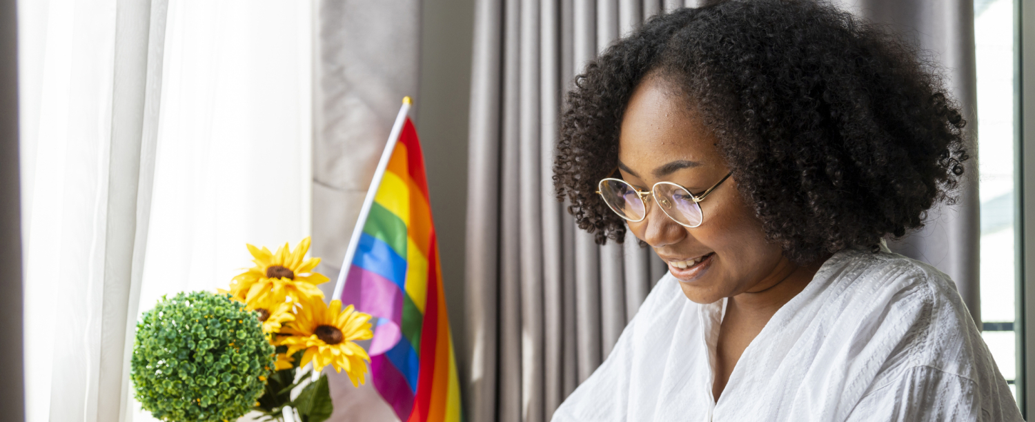 persoon die aan bureau zit met een regenboogvlagje op de achtergrond
